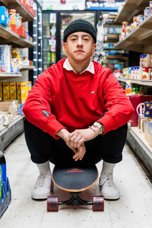 Non binary model wearing red sweater and beanie riding skateboard in convenience store